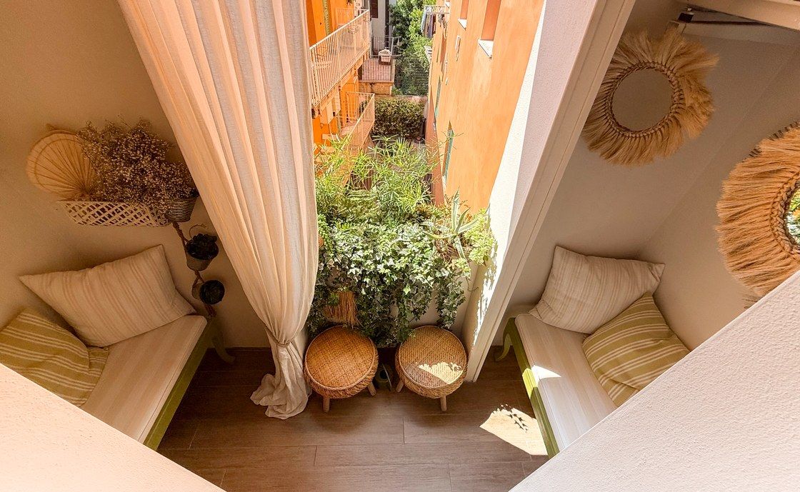 Balcony at Madonna del Terraglio with cushioned benches, a light curtain and round woven mirrors