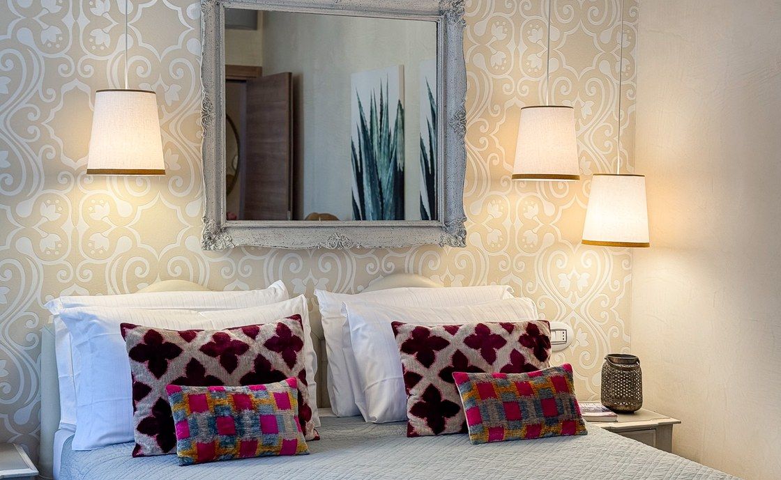 Bed at Madonna del Terraglio with a pale headboard, two wall lamps and a carved mirror