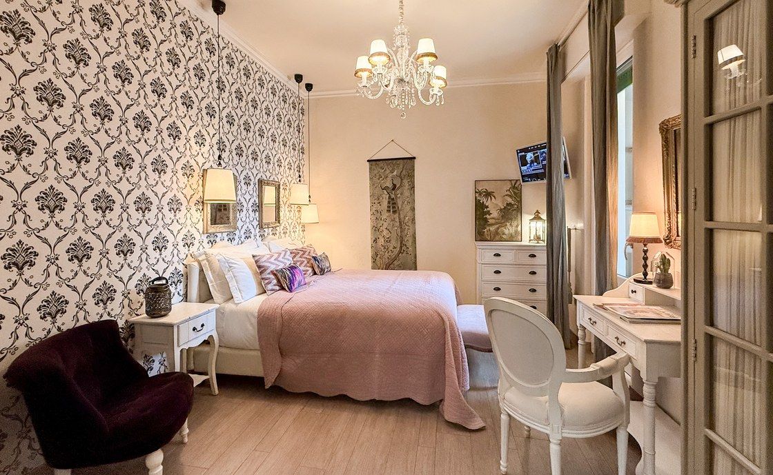 Bedroom at Madonna del Terraglio with damask wallpaper, a pink bedspread and a crystal chandelier