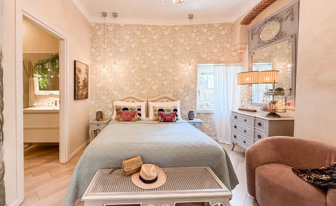 Bedroom at Santo Stefano with floral wallpaper and a sage green bedspread, the door open onto the bathroom