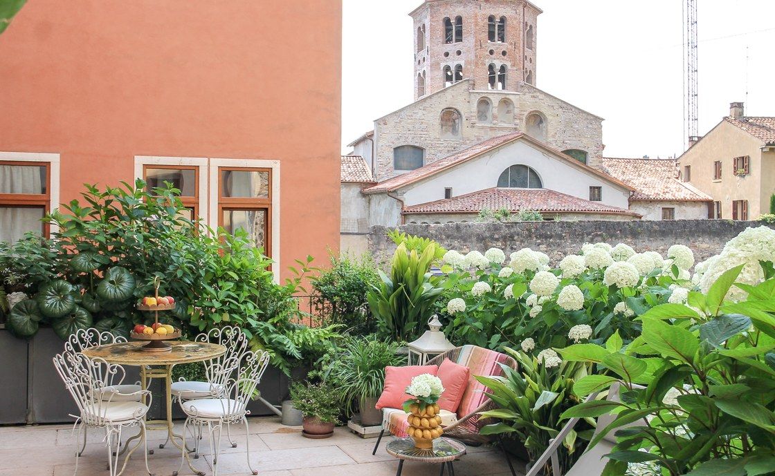 Santo Stefano's private terrace with a white wrought-iron table and chairs among hydrangeas, beneath a Romanesque bell tower